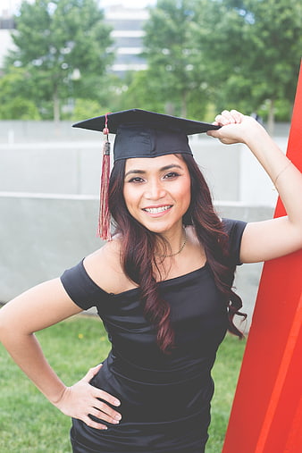 Smiling female graduate in black cap and gown holding tassel outdoors