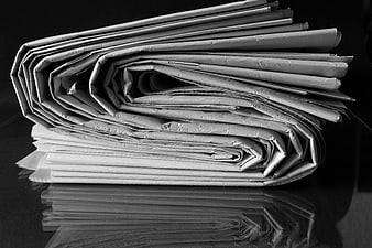 Stack of folded newspapers on a reflective black surface