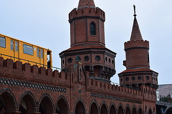 Yellow train crossing historic red brick bridge with towers