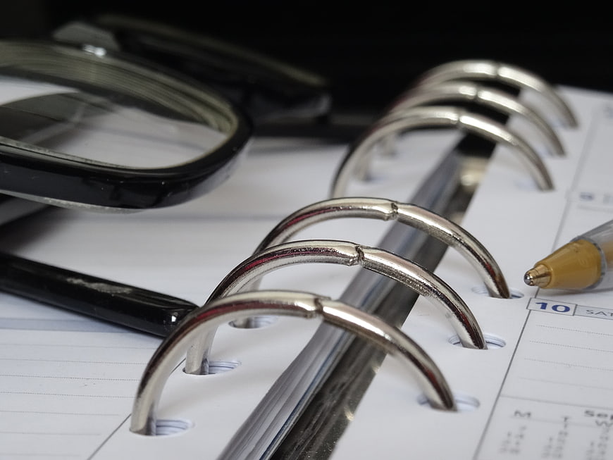 Close-up of binder rings, glasses, and pen on planner