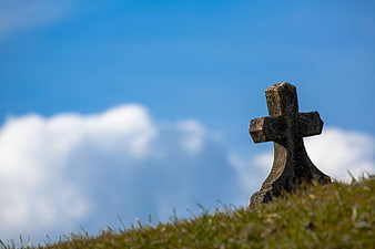 Old Stone Cross on Grassy Hill Against Blue Sky