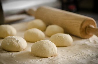 Homemade pizza dough balls with rolling pin on floured surface