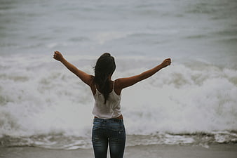Woman with arms raised facing ocean waves on beach