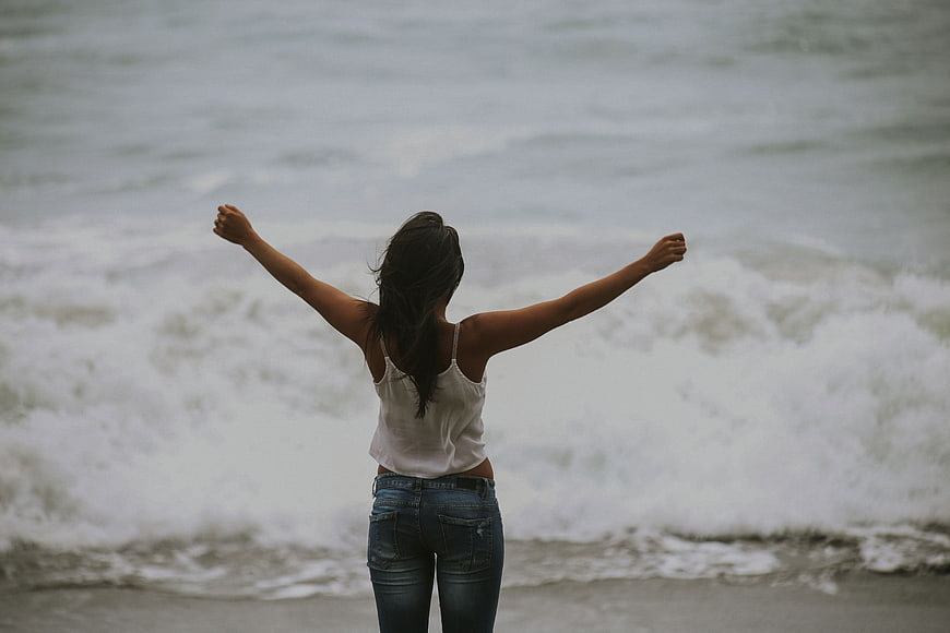 Woman with arms raised facing ocean waves on beach