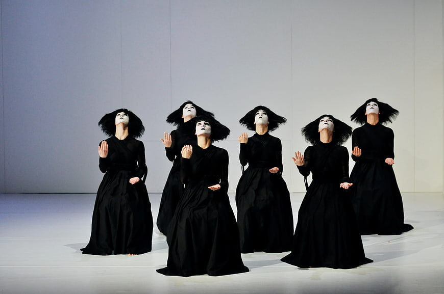 Group of dancers in black dresses and white masks performing