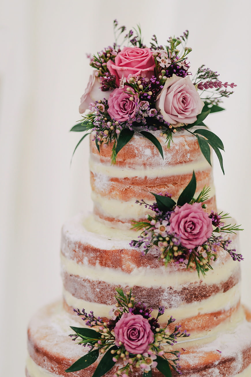 Three-tier semi-naked wedding cake with pink roses and greenery