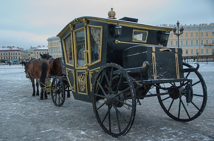 Historic black and gold horse-drawn carriage in snowy Palace Square, Saint Petersburg
