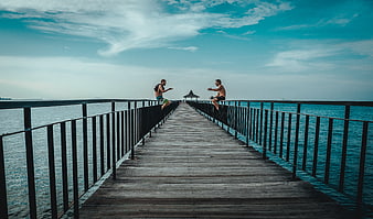 Two men sitting on pier railings talking over the sea