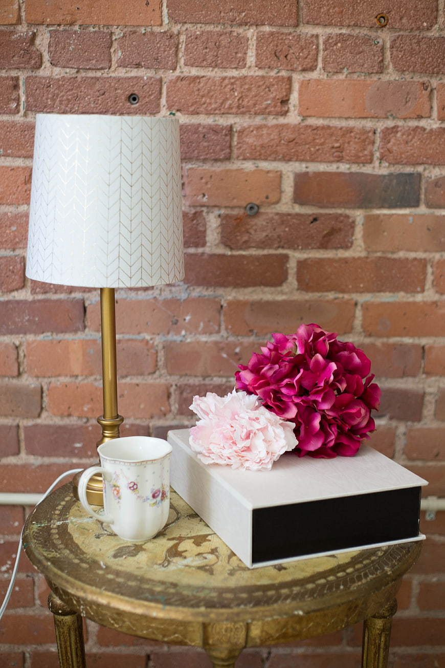 Vintage Table with Lamp, Peonies, and Mug against Brick Wall