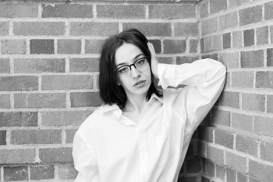 Black and white portrait of young woman with glasses against brick wall