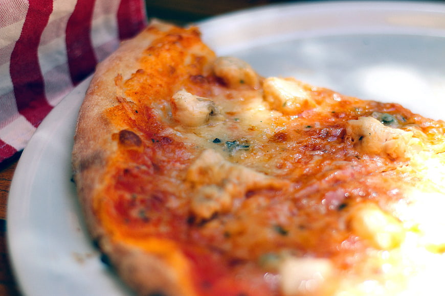Close-up of cheesy pizza slice on white plate