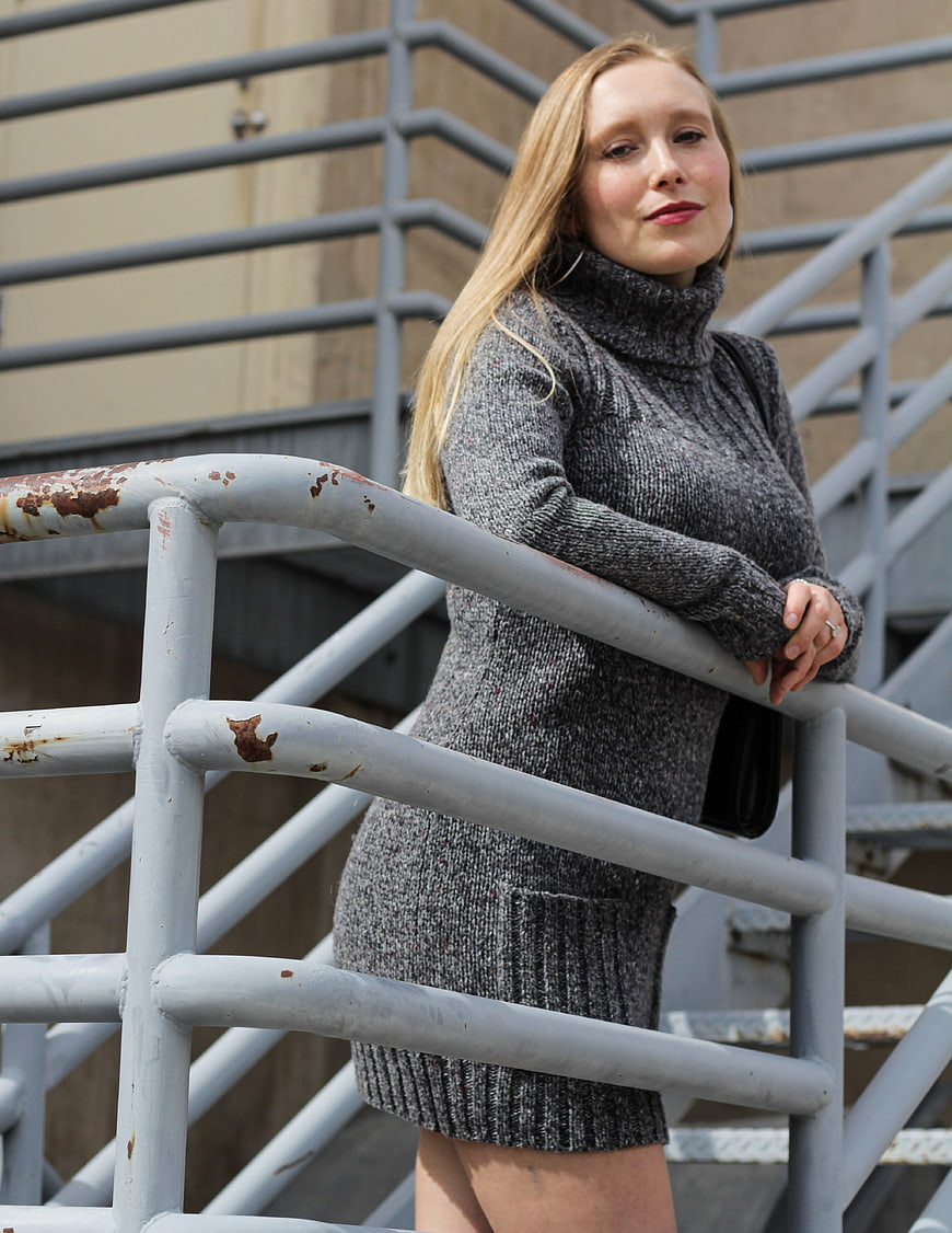 Young blonde woman in grey turtleneck sweater leaning on urban railing