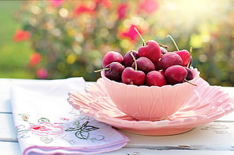 Fresh red cherries in a pink ceramic bowl on a white table