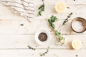 Flat lay of fresh herbs, lemons, and spices on white wood