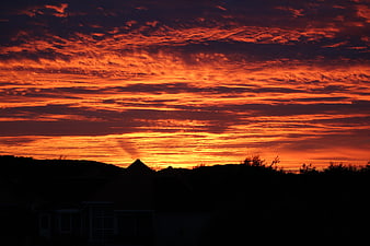 Dramatic fiery orange sunset sky with textured clouds over silhouette