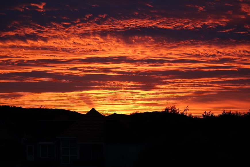 Dramatic fiery orange sunset sky with textured clouds over silhouette