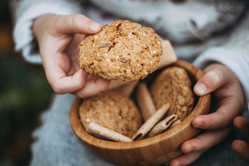 Hands holding oatmeal cookies in a wooden bowl