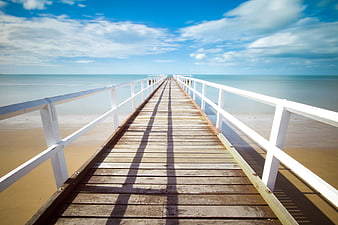 Wooden pier extending into calm ocean with blue sky