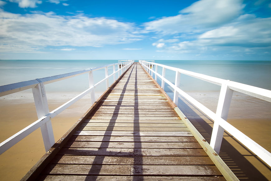 Wooden pier extending into calm ocean with blue sky