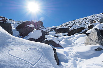 Heart drawn in snow on sunny mountain landscape