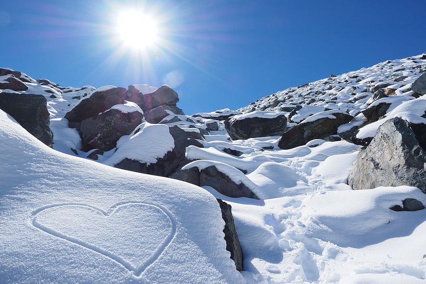Heart drawn in snow on sunny mountain landscape