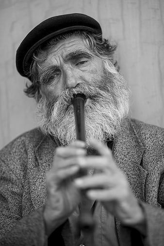 Black and white portrait of elderly bearded man playing kaval flute
