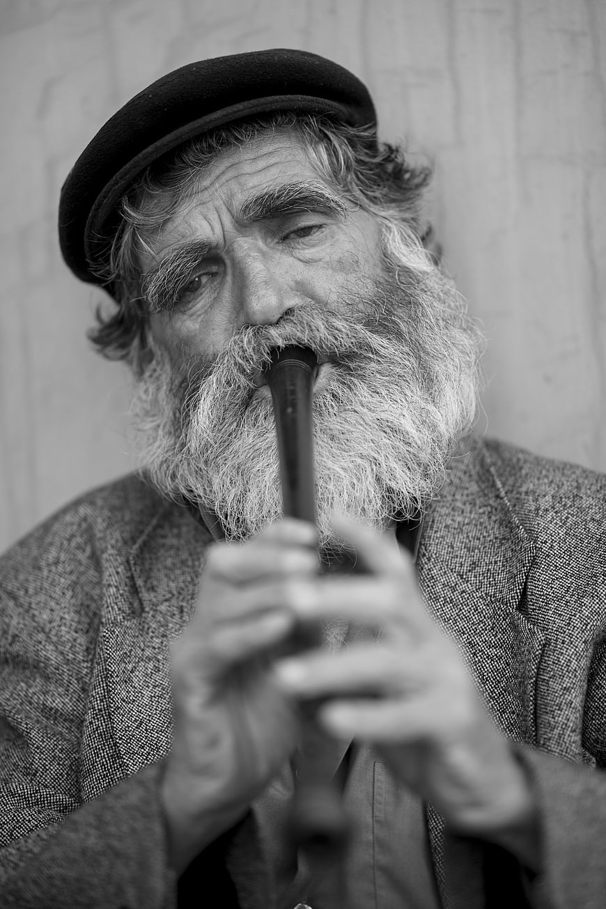 Black and white portrait of elderly bearded man playing kaval flute