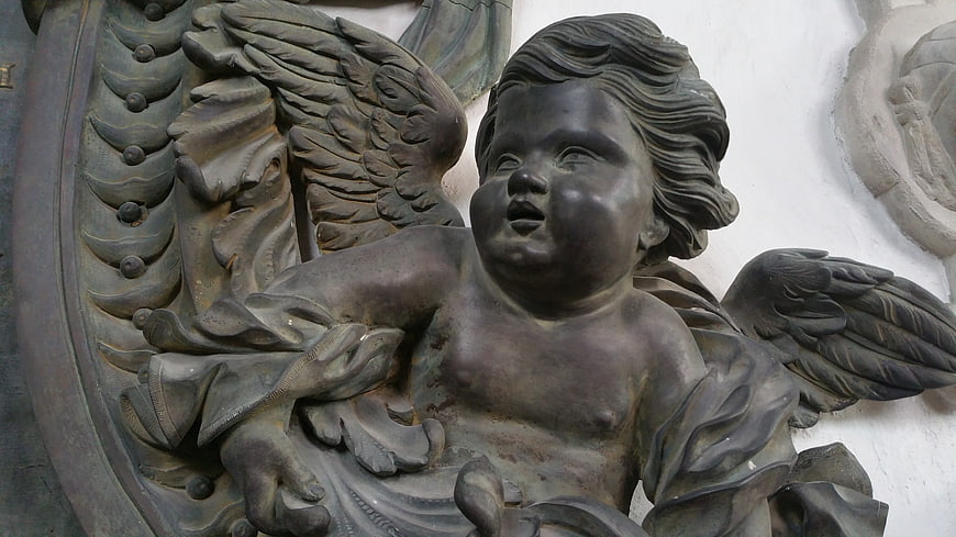 Close-up of dark bronze cherub sculpture with wings