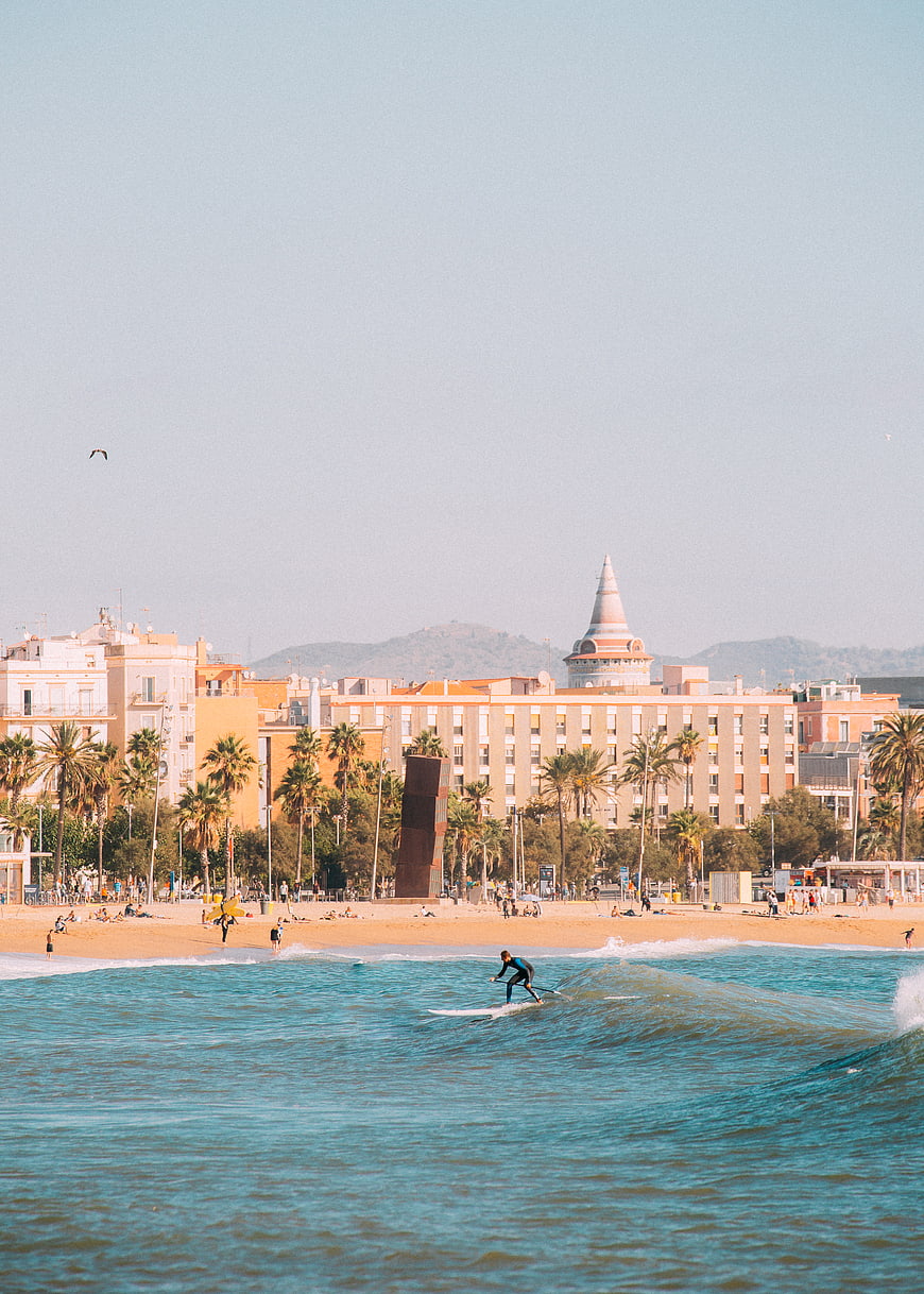 Surfer riding wave on sunny beach with city skyline