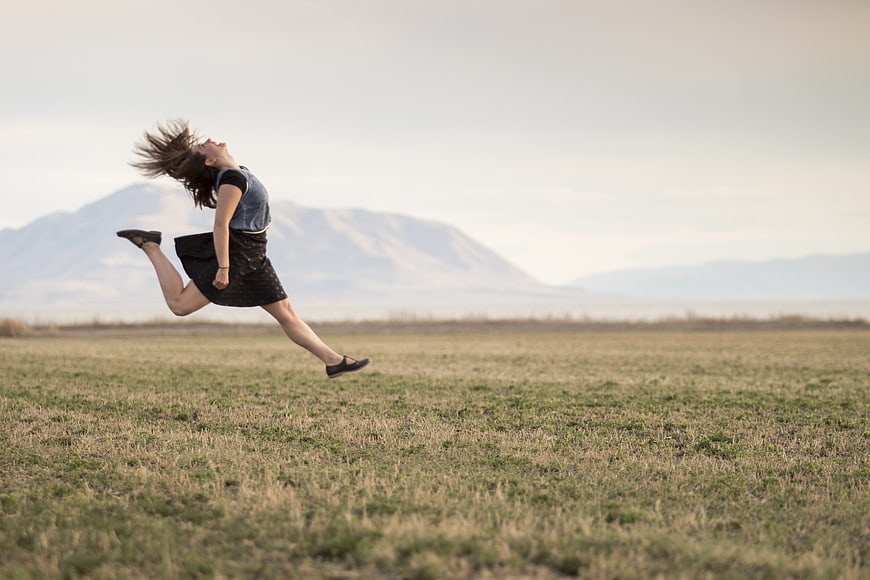 Woman jumping joyfully in open field with mountains