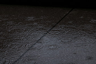 Raindrops creating ripples on wet asphalt pavement