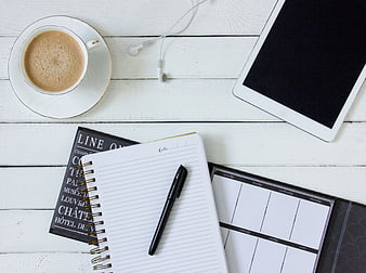 Flat lay of coffee, notebook, tablet, and headphones on white wood