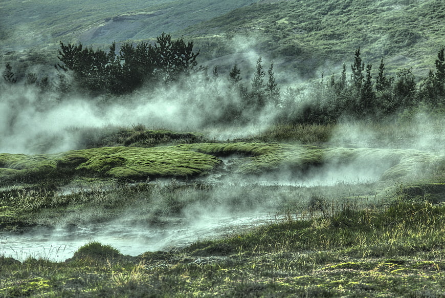Misty green landscape with steam rising from a geothermal stream