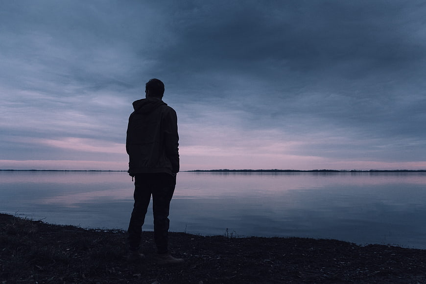 Silhouette of Man Standing by Lake at Dusk