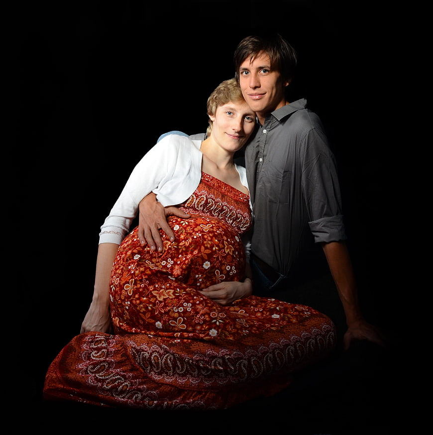 Pregnant couple sitting together on black background