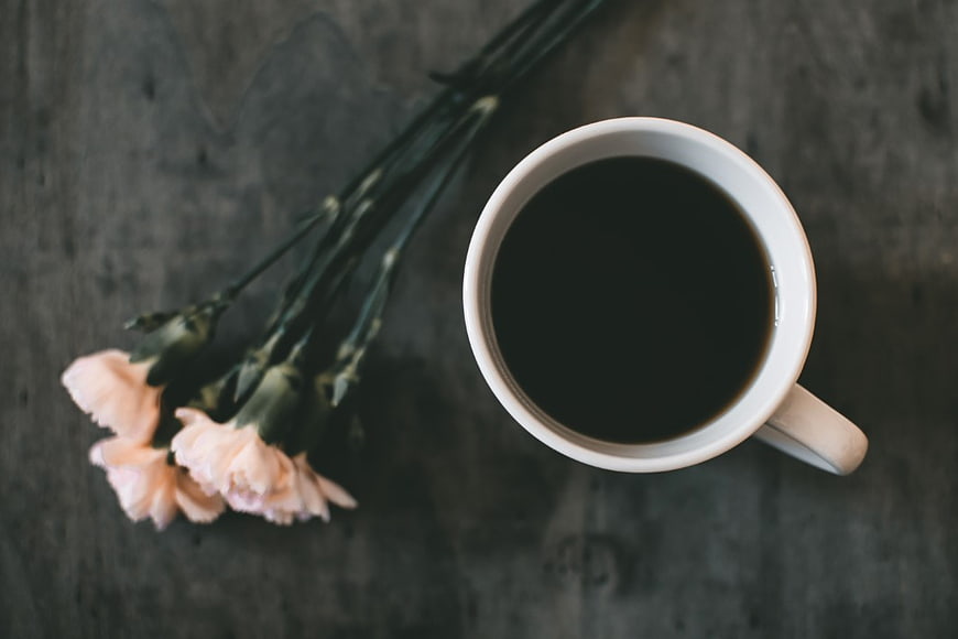 Top View of Black Coffee and Pink Carnations on Dark Table
