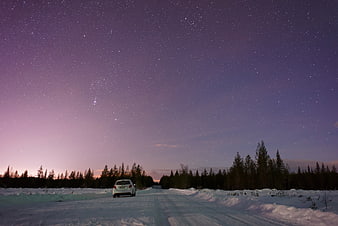 White car driving on snowy road under starry night sky