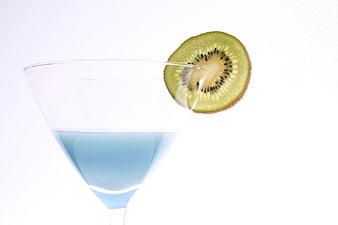 Blue cocktail in a martini glass with a fresh kiwi slice garnish on a white background