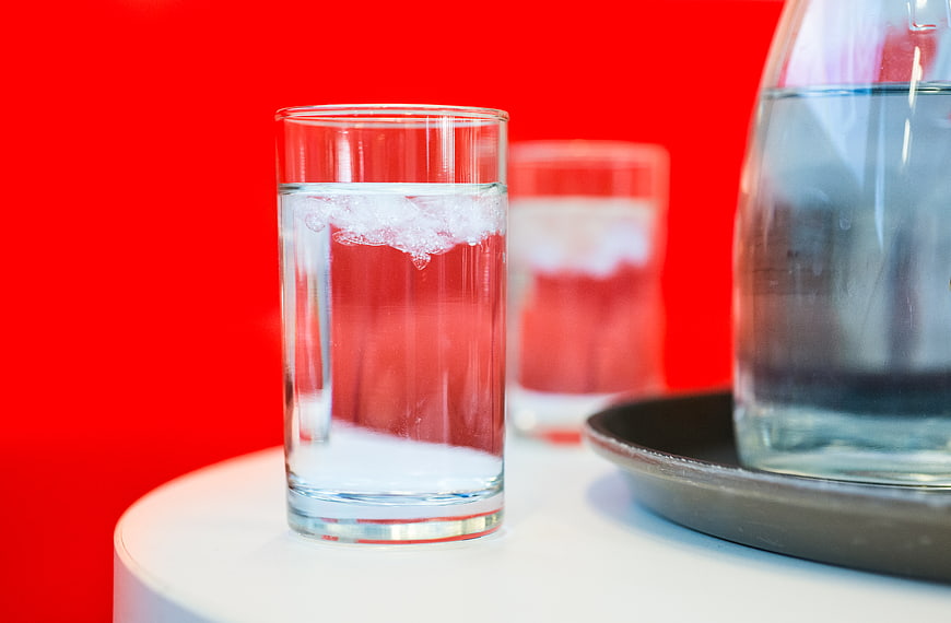 Glass of ice water on white table against red background