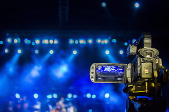 Professional video camera on tripod at concert with blue stage lights