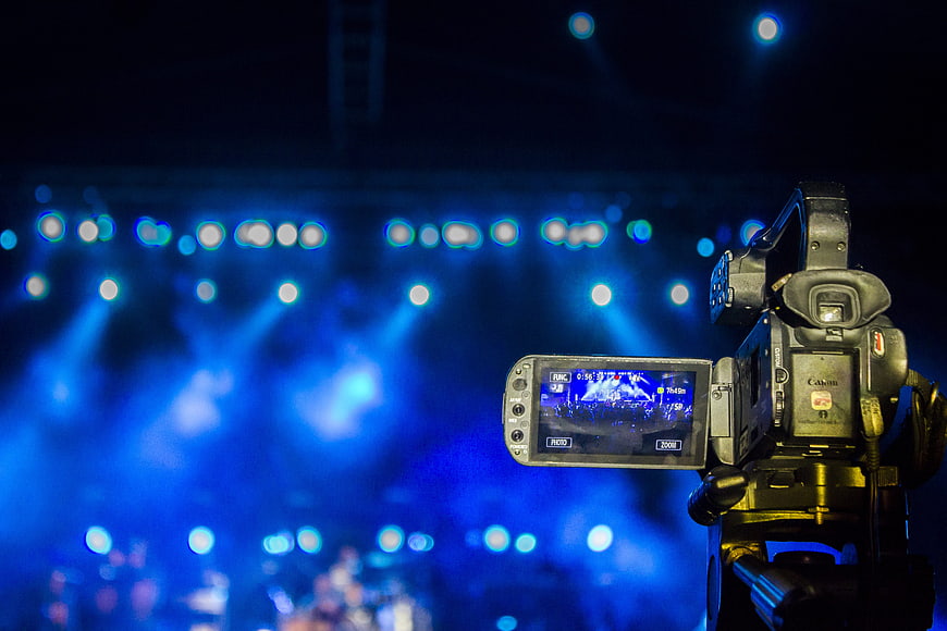 Professional video camera on tripod at concert with blue stage lights