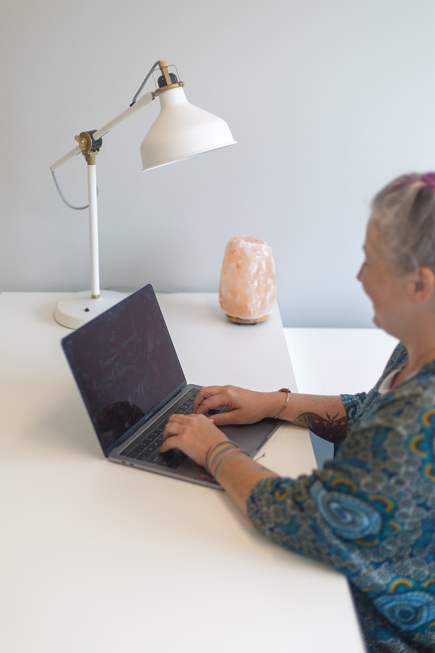 Senior woman typing on laptop at white desk with lamp
