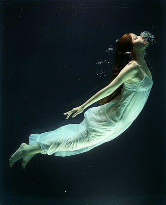 Woman in white dress floating underwater exhaling bubbles