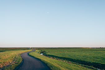 Winding Country Road Through Green Pastures Under Blue Sky