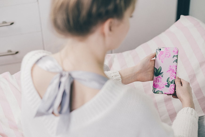 Woman holding floral smartphone case on striped bed