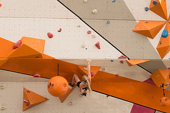 Woman climbing indoor bouldering wall with orange holds