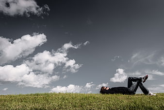 Man relaxing on grassy hill under dramatic cloudy sky