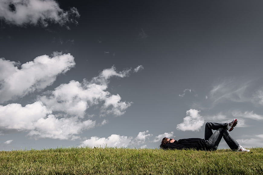 Man relaxing on grassy hill under dramatic cloudy sky