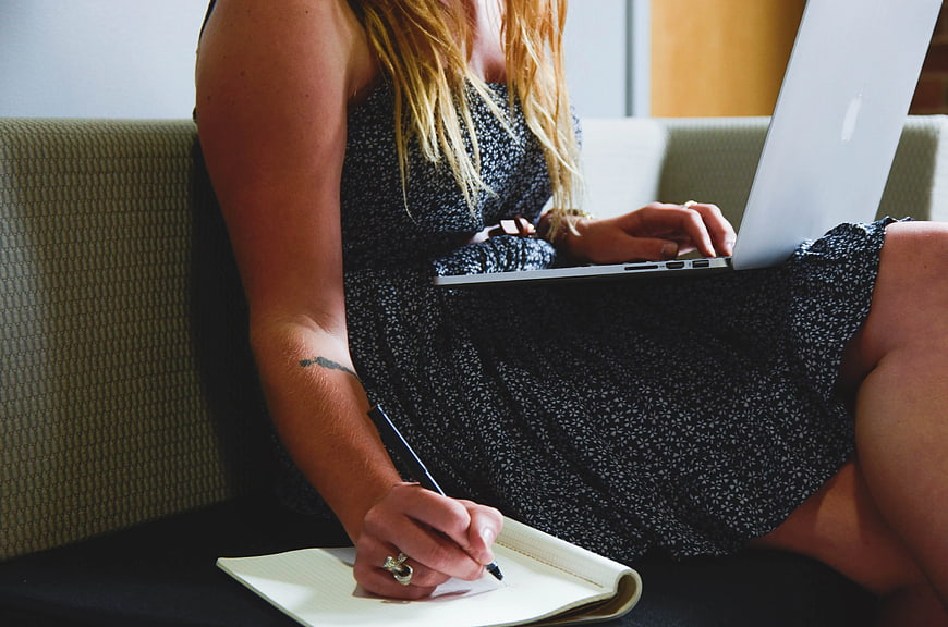 Woman Writing Notes While Using Laptop on Couch