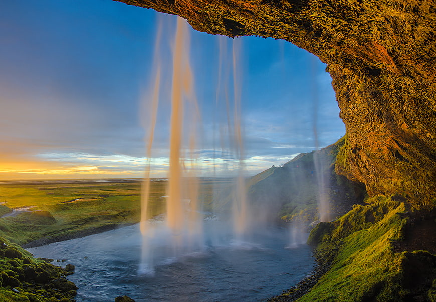 View from behind a waterfall at sunset with green landscape